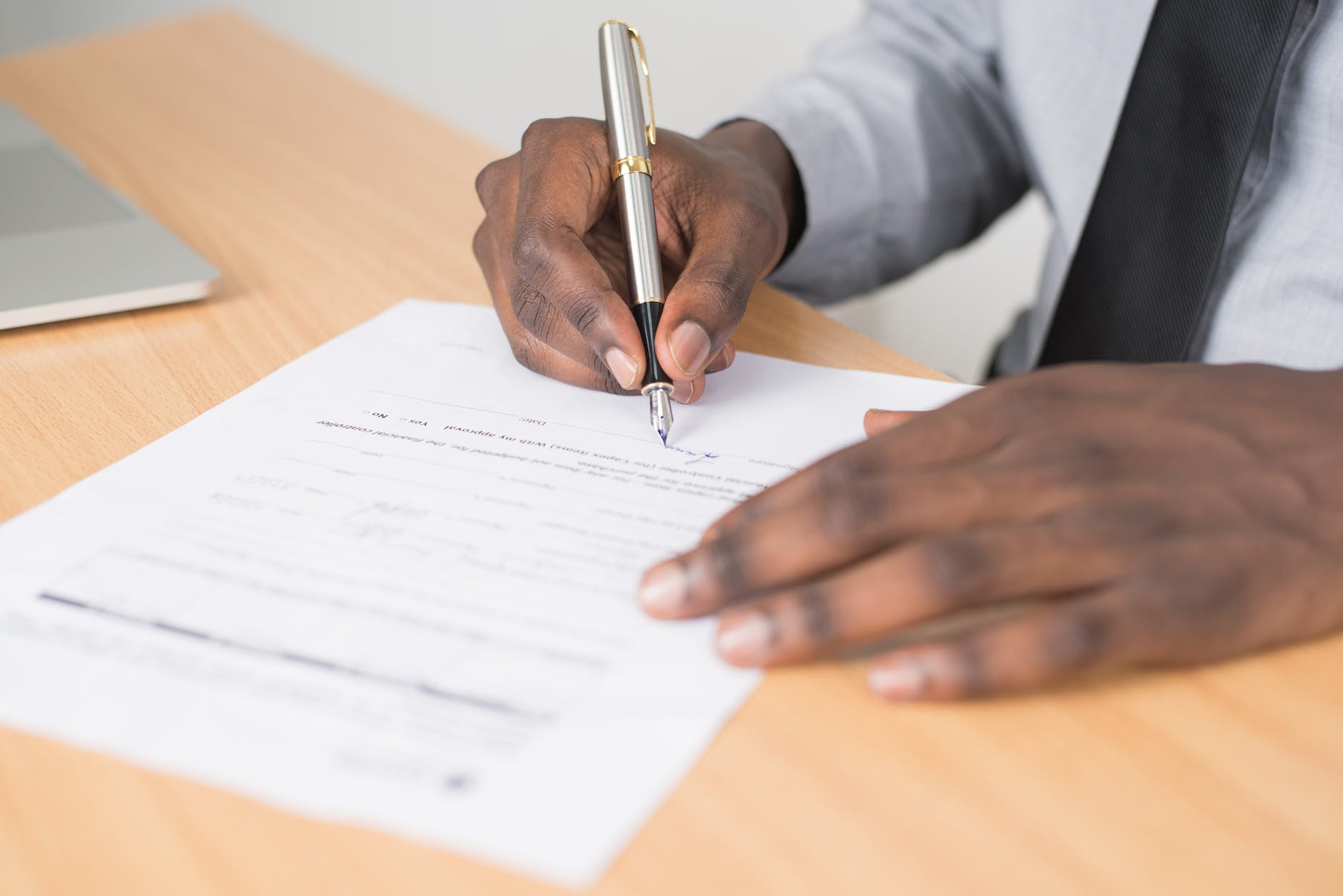 pexels-photo-955389 person holding gray twist pen and white printer paper on brown wooden table